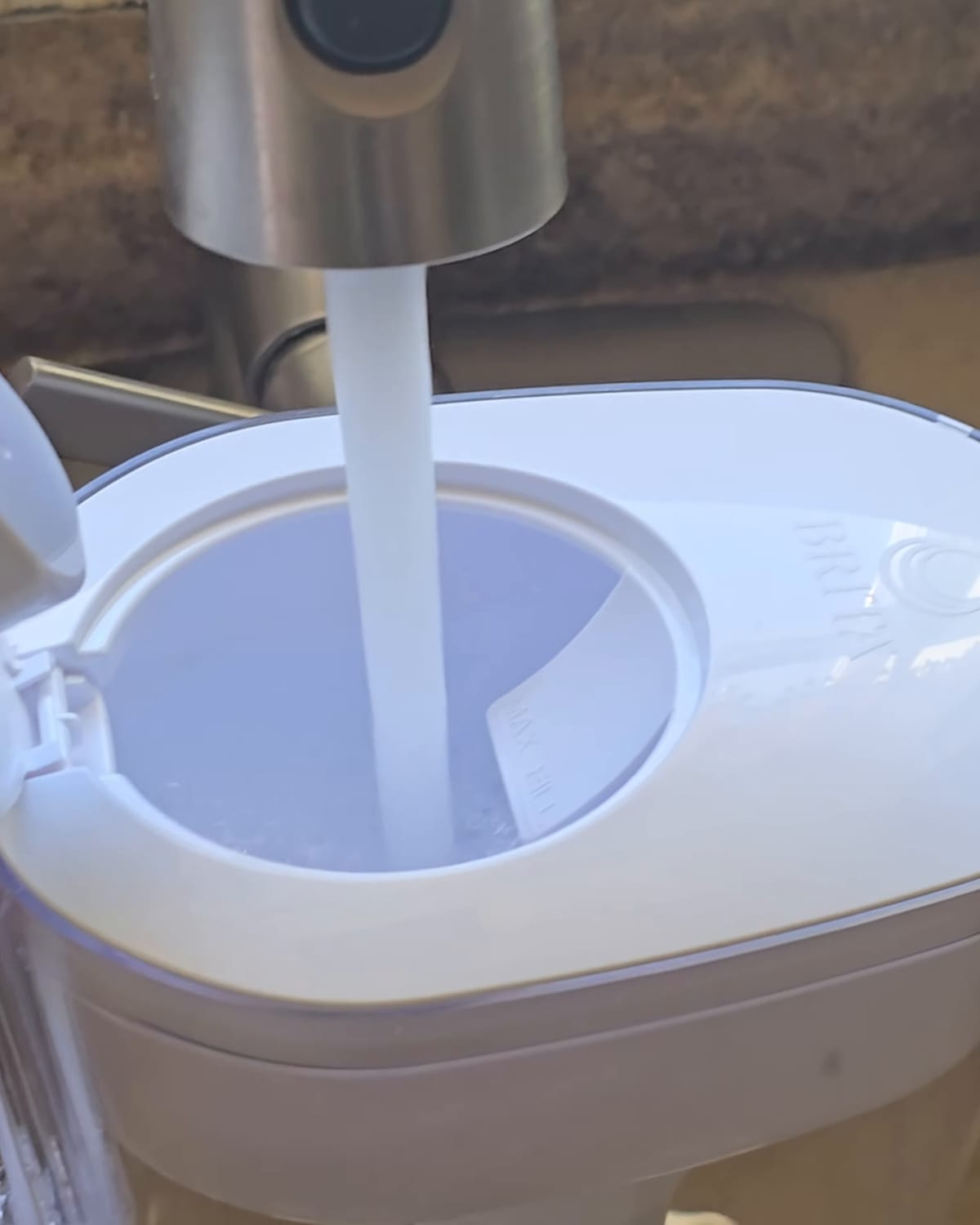 White water filter pitcher being filled from a kitchen tap